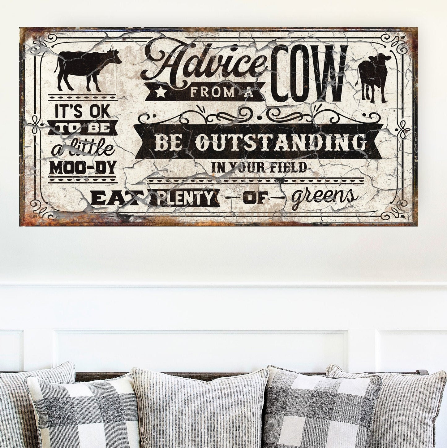 May include: A rustic white sign with black text and a distressed look. The sign reads 'Advice from a Cow: It's OK to be a little moo-dy. Be outstanding in your field. Eat plenty of greens.' The sign features a black silhouette of a cow in the top left corner and a black silhouette of a calf in the top right corner.