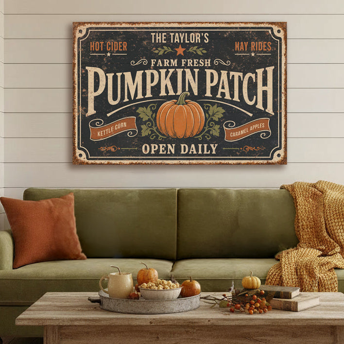 A rustic canvas sign reading 'The Taylor's Pumpkin Patch Open Daily' hangs above an olive green sofa in a styled living room with a coffee table, pillows, and fall decor.