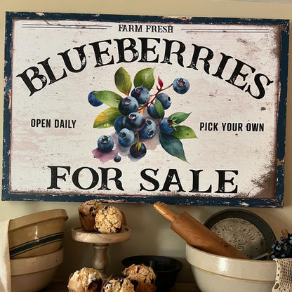 Vintage-style 'Blueberries For Sale' sign on a rustic shelf with muffins and kitchenware.