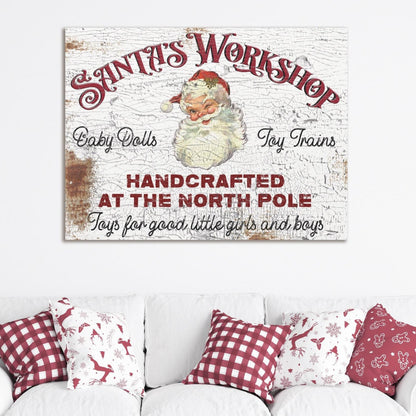 May include: A vintage white canvas sign with red text that reads &#39;Santa&#39;s Workshop&#39; with a picture of Santa Claus. The sign also reads &#39;Baby Dolls&#39;, &#39;Toy Trains&#39;, &#39;Handcrafted at the North Pole&#39;, and &#39;Toys for good little girls and boys&#39;. The sign is hanging on a white wall above a white couch with red and white checkered pillows.