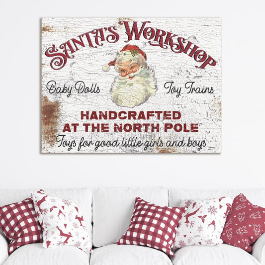 May include: A vintage white canvas sign with red text that reads &#39;Santa&#39;s Workshop&#39; with a picture of Santa Claus. The sign also reads &#39;Baby Dolls&#39;, &#39;Toy Trains&#39;, &#39;Handcrafted at the North Pole&#39;, and &#39;Toys for good little girls and boys&#39;. The sign is hanging on a white wall above a white couch with red and white checkered pillows.